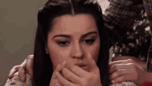 a woman is covering her mouth with her hands while sitting on a bed .