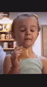 a little girl is holding a piece of food in her hand .