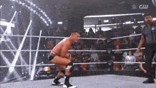 a wrestler is squatting down in a wrestling ring with a cw logo in the background