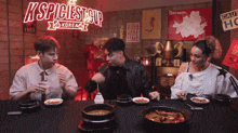 three people are sitting at a table with bowls of food in front of a sign that says ' k spiciest cup korea '