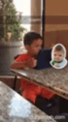 a young boy is sitting at a table with a tablet and a picture of a baby on it .