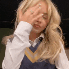 a woman wearing a white shirt and a blue vest is covering her face