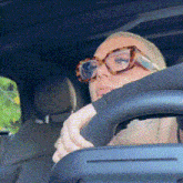 a woman wearing glasses is driving a car with her head resting on the steering wheel