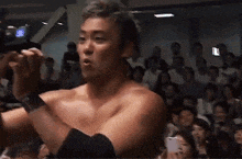 a man without a shirt is standing in front of a crowd in a gym .