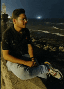 a man wearing glasses sits on a wall looking at the ocean