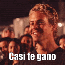 a man is smiling in front of a crowd and the words casi te gano are on his face .
