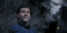 a man in a blue jacket is standing in front of a tree