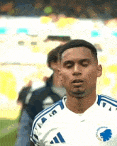 a soccer player wearing a white and blue adidas jersey looks down