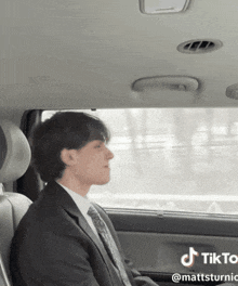 a man in a suit and tie is sitting in the back seat of a car with tiktok written on the bottom