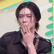 a man with long black hair is wearing a ring on his finger and covering his mouth with his hand .