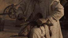 a man in a white robe is cutting a piece of wood with a knife