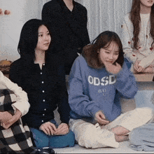 a group of young women are sitting on the floor and one of them is wearing a blue sweatshirt that says odsd .