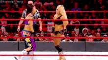 two women are wrestling in a wrestling ring while a referee looks on .