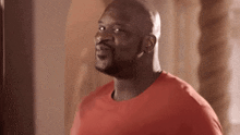 a bald man in a red shirt is standing in front of a punching bag and smiling .