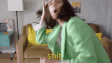 a woman in a green jacket is sitting on a couch with her mouth open and the word shit written in yellow .