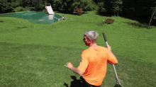 a man in an orange shirt is holding a rake in front of a water slide