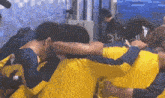 a group of people in yellow shirts are hugging each other in a room .
