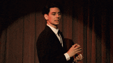 a man in a tuxedo is holding a deck of playing cards in front of a red curtain