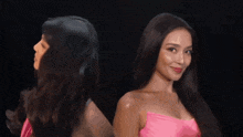 two women are standing next to each other in front of a black background . one is wearing a pink dress .