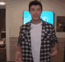 a man wearing a plaid shirt and a white shirt is standing in front of a television .