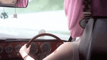 a girl with pink hair is driving a car with a sticker on the rear view mirror that says ' miku '