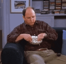 a man is sitting on a couch with a bowl of popcorn in his hand .