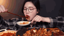 a woman wearing glasses is eating food from a bowl with chopsticks