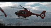 a red helicopter is flying in the sky with a white and red tail