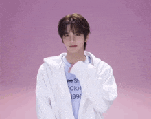 a young man wearing a white jacket and a blue shirt is standing on a pink background .
