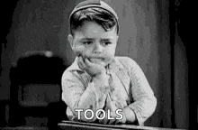 a black and white photo of a boy sitting at a desk with his hand on his chin and the words `` tools '' .