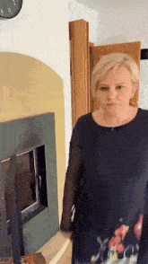 a woman in a black dress is standing in front of a fireplace with a clock on the wall
