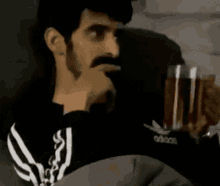 a man with a beard is sitting on a couch holding a glass of red liquid