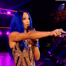 a woman with blue hair is holding a microphone and a ring that says reign