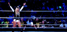 a woman stands in a wrestling ring with her hands in the air