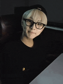 a young man wearing glasses and a hat is sitting in front of a keyboard
