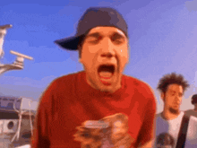a man wearing a red shirt and a baseball cap is making a funny face