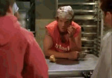 a man wearing a red shirt that says ' pe ' on it is smoking a cigarette in a kitchen .