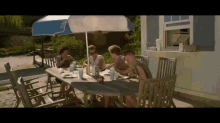 a group of people are sitting at a table under a blue and white umbrella