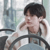 a young man is sitting in the driver 's seat of a bus and looking out the window .