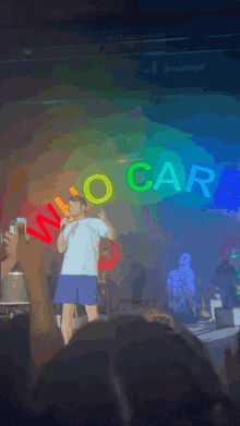 a man stands on stage in front of a neon sign that says neo car