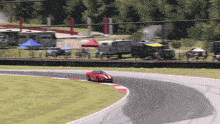 a red race car is going around a curve on a track with a trailer in the background
