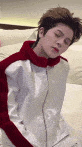 a young man wearing a white jacket with red stripes on the sleeves is sitting on a bed with his eyes closed