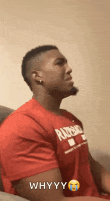 a man in a red shirt is sitting on a couch and says why yy