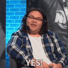 a man wearing headphones and a plaid shirt says " yes "