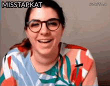 a woman wearing glasses and a colorful shirt is smiling and says misstapkat .