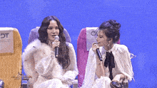 two women are sitting next to each other and one is singing into a microphone with the word dt on the back