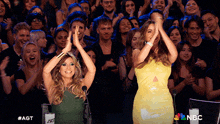 two women applaud in front of a crowd with the nbc logo