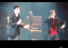 a man in a red shirt is singing into a microphone on stage