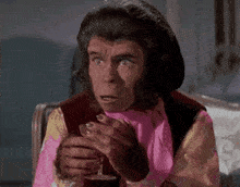 a chimpanzee is holding a glass of wine in his hand .