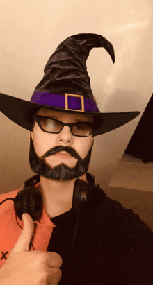 a man with a beard wearing a witch hat and headphones gives a thumbs up